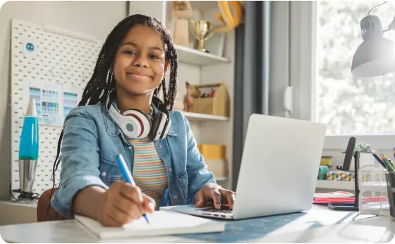 Middle school student taking notes at home while working with her laptop