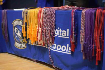 Colorful graduation cords are neatly arranged on a blue tablecloth with a logo, evoking a sense of achievement and celebration.