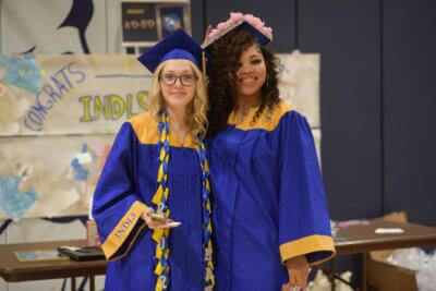 Two graduates in blue and gold gowns and caps stand smiling.
