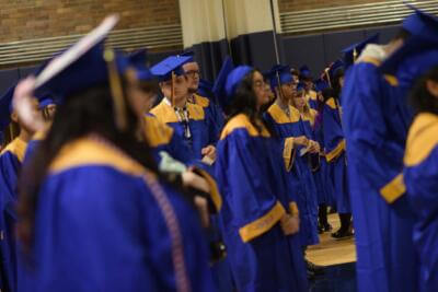 A group of graduates in blue and yellow gowns and caps stands indoors, capturing a sense of accomplishment and anticipation in a formal ceremony setting.