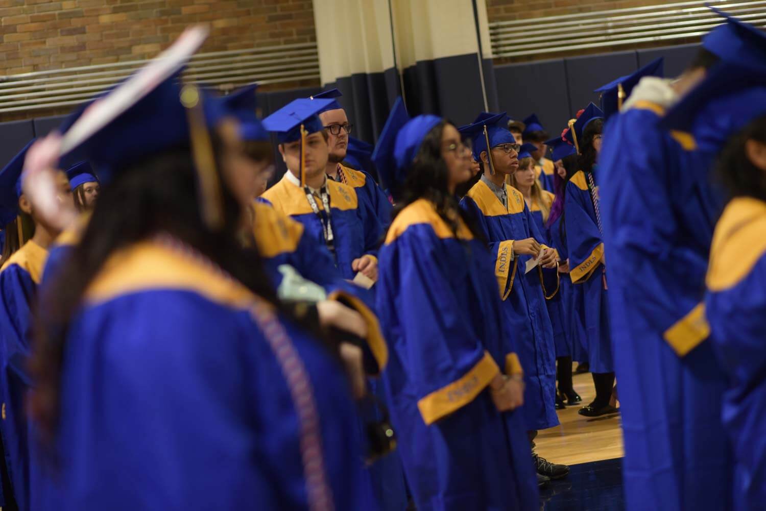 A group of graduates in blue and yellow gowns and caps stands indoors, capturing a sense of accomplishment and anticipation in a formal ceremony setting.
