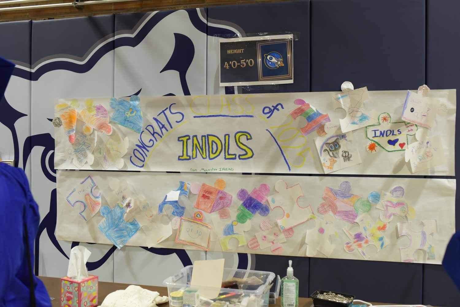 Colorful congratulatory banner with drawings and cut-out shapes displayed on a wall.